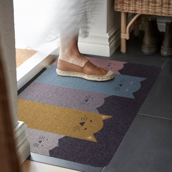 Person on colourful cat-themed doormat near door and shoe bench.