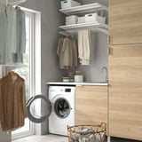 Small laundry room with white UDDARP washer/dryer, open door, wooden shelves with clothes, gray walls.