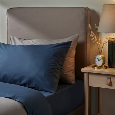 Bed with blue ULLVIDE pillow, textured headboard, bedside clock & dried flowers.