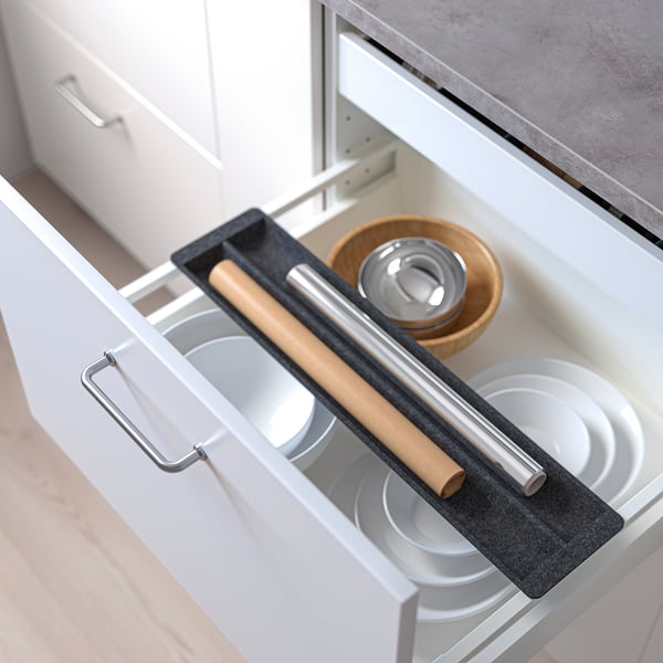 Open kitchen drawer with sliding organizer holding plates, rolling pin, and bowls. Organizer creates extra storage and dampens sound.
