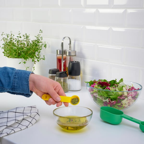 Measuring and pouring seasoning into oil, salad bowl and spoons nearby.