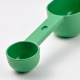 Bright green measuring spoon, part of a set, resting on a white surface. Clear, high-quality plastic with embossed markings for precise measurements.