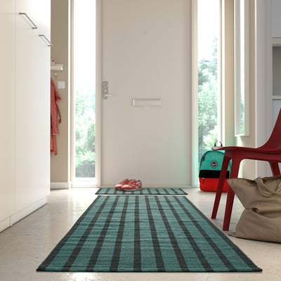 Blue-green and black striped rug near door, beside red chair.