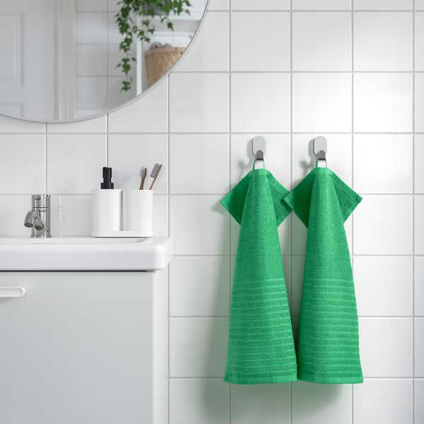 Green VÅGSJÖN towels on hooks in modern bathroom, absorbent cotton.