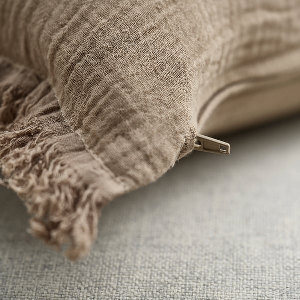 Soft, beige cushion cover with zipper, made from 100% cotton muslin, featuring crinkled texture and raw edges for a casual look.