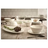 Table display with VARDAGEN white dishes, including bowls, plates, and cups. Glass and ceramic materials, classic round design, set on a wooden table.