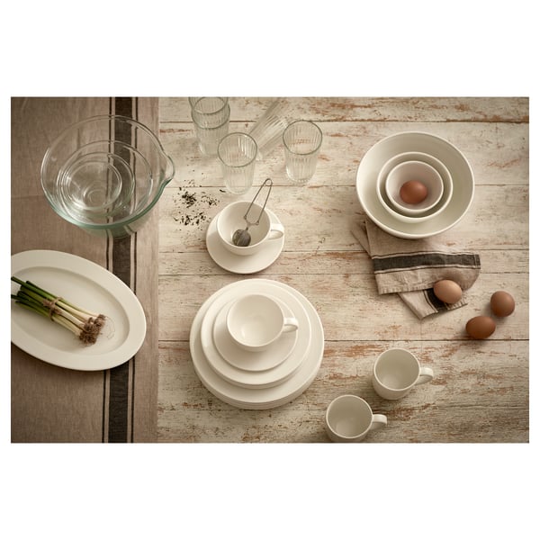 VARDAGEN white dishware set. It includes plates, cups, bowls, and glasses on a wooden table. The items are simplistic, round, and timeless in design.