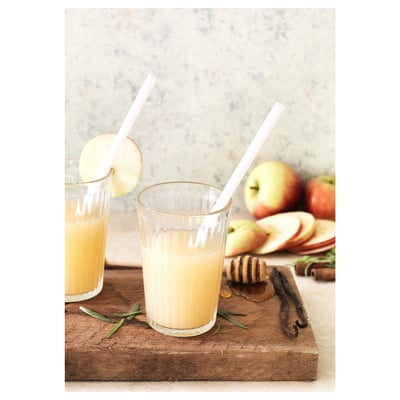 Two clear, pleated glasses with light yellow liquid and straws on a wooden board with apples.