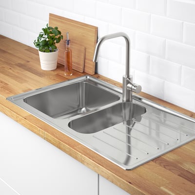 Stainless steel kitchen sink with drainboard and faucet on wooden countertop, next to a plant.