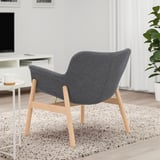 Dark grey armchair with wooden legs and gold accents on a speckled rug in a minimalist living room.