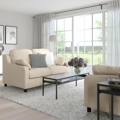 Modern living room with VINLIDEN beige sofa, black coffee table, side table, rug, and flower vase. Large windows with sheer curtains.