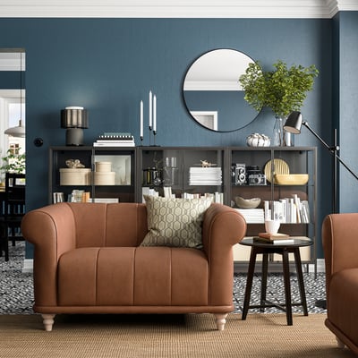 Luxurious living room with deep brown fabric VISKAFORS armchair, patterned carpet, dark blue walls, and decorative shelves with books and plants.