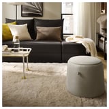Modern living room with black sofa, white shaggy rug, and oval ottoman. Accented with pillows, a side table, and a cozy blanket.