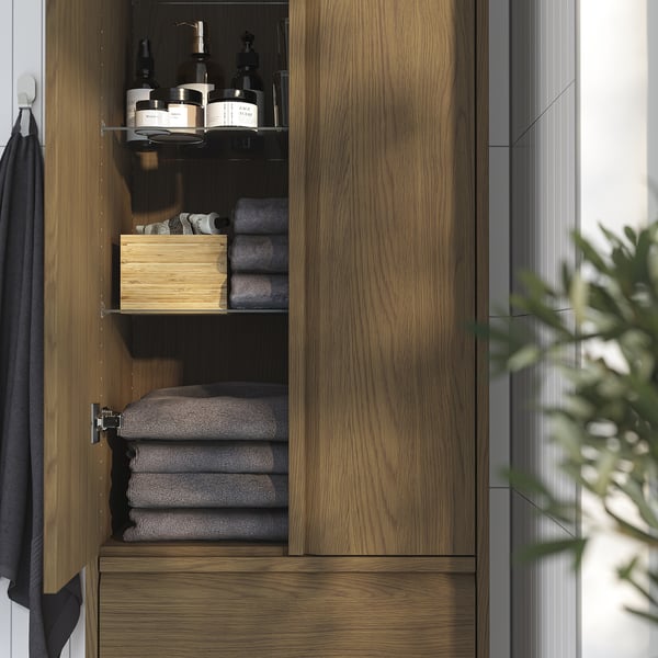 Puinen kylpyhuoneen kaappi hyllyillä ja laatikoilla. Säilyttää pyyhkeitä ja hygieniatarvikkeita. Integroidut kahvat takaavat modernin ilmeen.