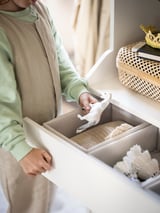 Nainen purkaa BAXNA-harmaan järjestäjän pakkauksesta, beigen ja kerman sävyistä.