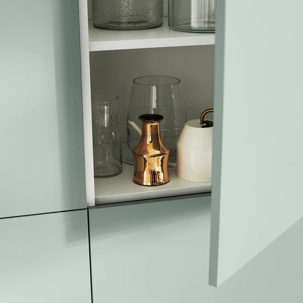 Vaaleansininen BESTÅ-hylly, jossa on lasiesineitä ja pronssinen maljakko.