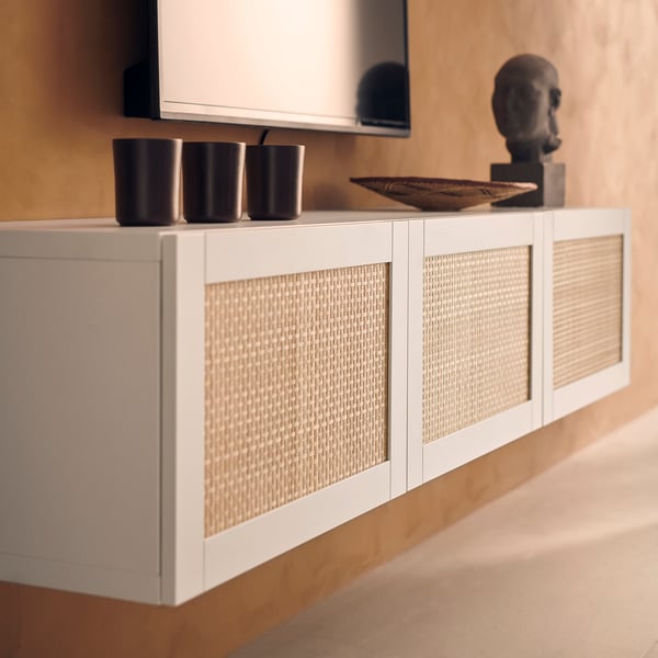 Moderni valkoinen tv-taso, jossa on kudottuja paneeleja, kolme mustaa kuppia ja koristeveistos.