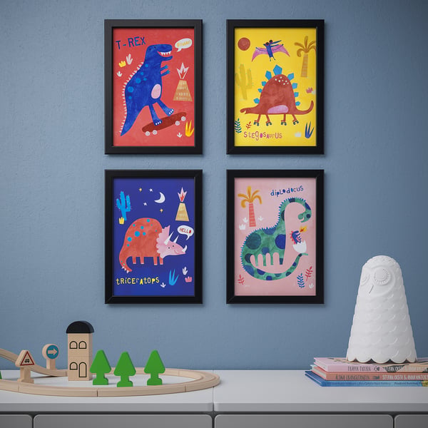 Neljä dinosaurusprinttiä mustissa kehyksissä harmaalla seinällä. Alla on lelujunasarja, jossa on vihreitä puita ja puutaloja. Oikealla kirjoja ja valkoinen pöllölamppu.