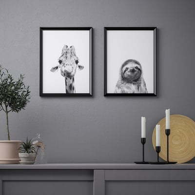 Kehystetyt kirahvi- ja laiskiaisprintit hyllyn yläpuolella kasveilla, kynttilöillä, lautasella.