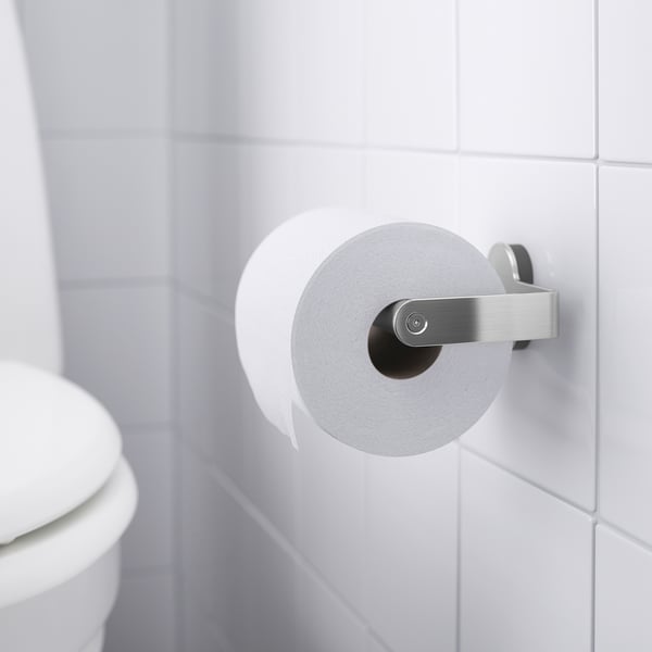 Valkoinen wc-paperiteline, joka on kiinnitetty valkoiselle kaakeloidulle seinälle, jossa on wc-paperirulla, osa BROGRUND-sarjaa piiloruuveilla.