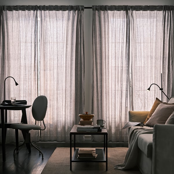 Kuvan kuvaus: huone, jossa on läpikuultavat pellavaverhot, jotka päästävät hajavaloa. Työpöytä tuolilla ja sohva tyynyineen ja peittoineen.