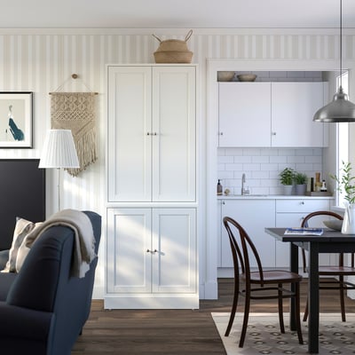 Moderni keittiö, jossa valkoiset kaapit, tummansininen tuoli, boho-koristeet ja musta pöytä ruskeilla tuoleilla.