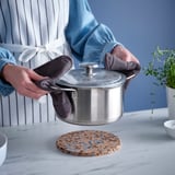 Kädet, joissa on hanskat, asettavat kannen pannunalustalle. Siniset pisteet korkissa keittiössä.