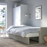 Sininen makuuhuone, jossa valkoinen sänky, harmaa matto, kasvi ja kori.