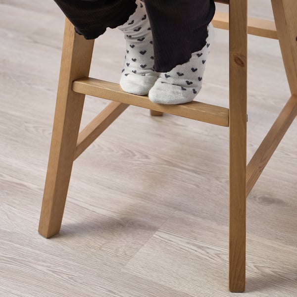 Lapsi istuu juniorituolilla, joka on suunniteltu ruokapöydän korkeuteen. Tuolissa on näkyvät puiset jalat ja jalkatuki tukena.