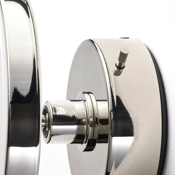 Hopeanvärinen seinävalaisin, jossa on tyylikäs, pyöristetty muotoilu ja metallipinta. Sivulla näkyy pieni himmennyspainike.