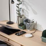 Puinen työpöytä, jossa on kannettava tietokone, älypuhelin, lamppu, kasvi, paperitavarat ja pieni, pyöreä, valkoinen langaton latausalusta LIVBOJ:lta.