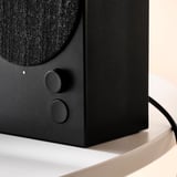 Musta bluetooth-kaiutin kangaspäällysteellä, säätimet, jalustalla.