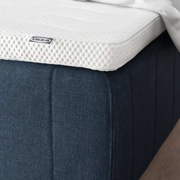 Patja, jossa on vahvistetut reunat ja IKEA-lappu tummansinisellä pohjalla, tukemassa selkärangan linjausta.