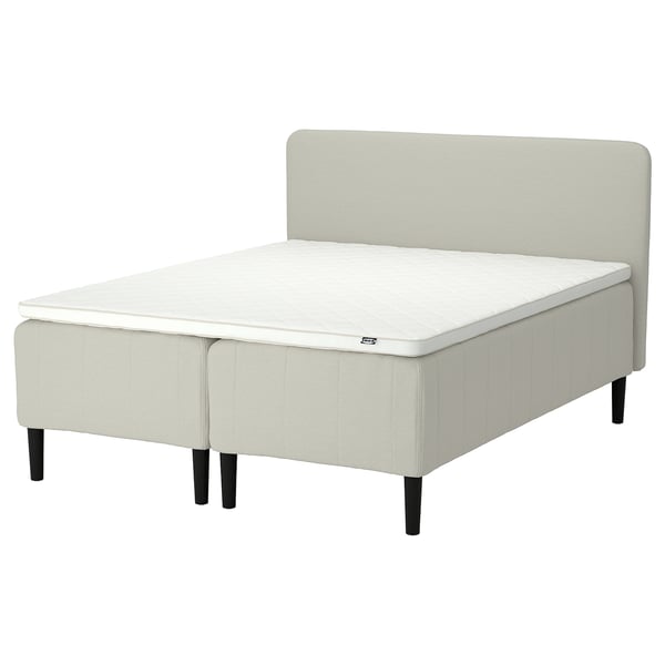 Moderni beige sänky valkoisella patjalla, pehmustettu sängynpääty, tumma puujalka.