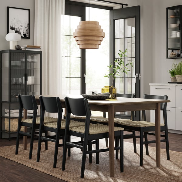 Moderni jatkettava pöytäsarja, kudotut tuolit, tyylikäs matto, riippuvalaisin, hyllyt kasveilla ja kirjoilla.