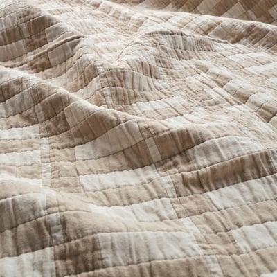 Taitettu beige ja valkoinen ruudullinen peitto, jossa on pehmeä rakenne.