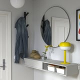 Moderni eteinen harmaalla seinällä, hyllyssä farkkutakki, lamppu, kukkia, peili ja säilytystilaa.