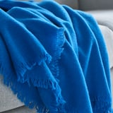 Kirkkaan sininen peitto valkoiselle sohvalle verhottuna, joka esittelee sen pehmeää, muhkeaa tekstuuria ja hapsujen yksityiskohtia.