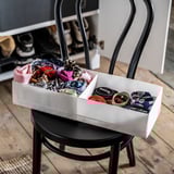 Valkoinen säilytyslaatikko mustalla tuolilla, jossa on värikkäitä vaatteita ja rullattuja vöitä.