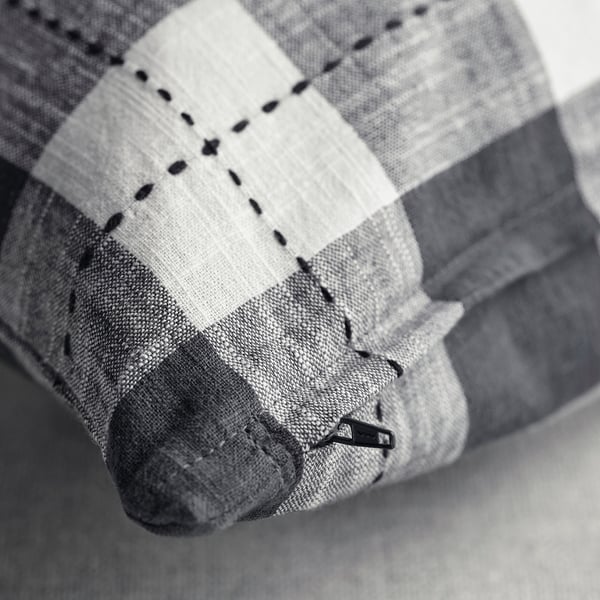 Mustavalkoinen tyynynpäällinen, jossa on perinteinen ruudullinen kuvio, jossa näkyvät ompeleet ja vetoketju.