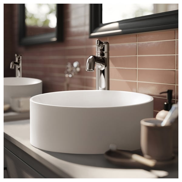 Moderni kylpyhuone, jossa on pyöreä valkoinen marmorinen pesuallas, kromihana ja saippua-annostelija.