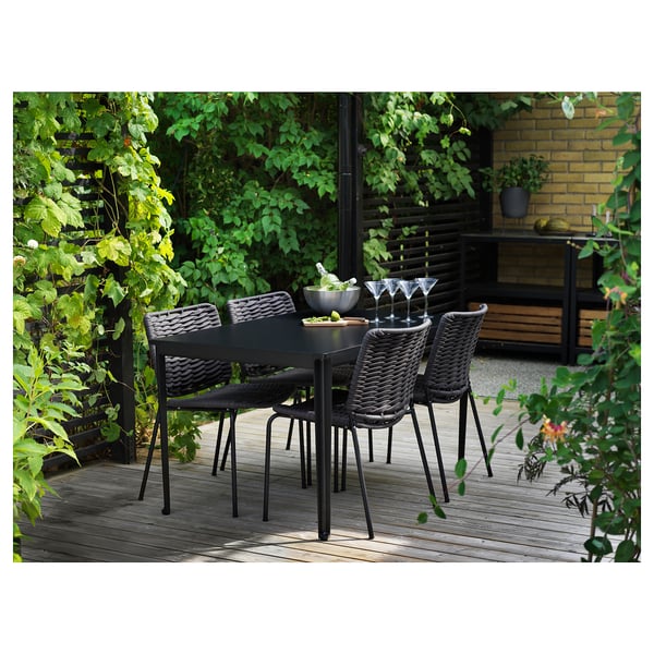 Moderni musta ulkopöytä, jossa on neljä yhteensopivaa tuolia puisella terassilla vihreiden kasvien ympäröimänä.