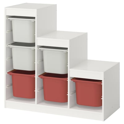 Valkoinen ikea TROFAST -säilytyskaappi punaisilla ja valkoisilla muovilaatikoilla. Siinä on kolme hyllyä, joissa on porrastettu muotoilu.
