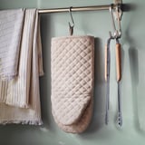 Beige VÄLVÅRDAD-uunikinnas kaiteella, jota reunustavat pyyhkeet ja pihdit.