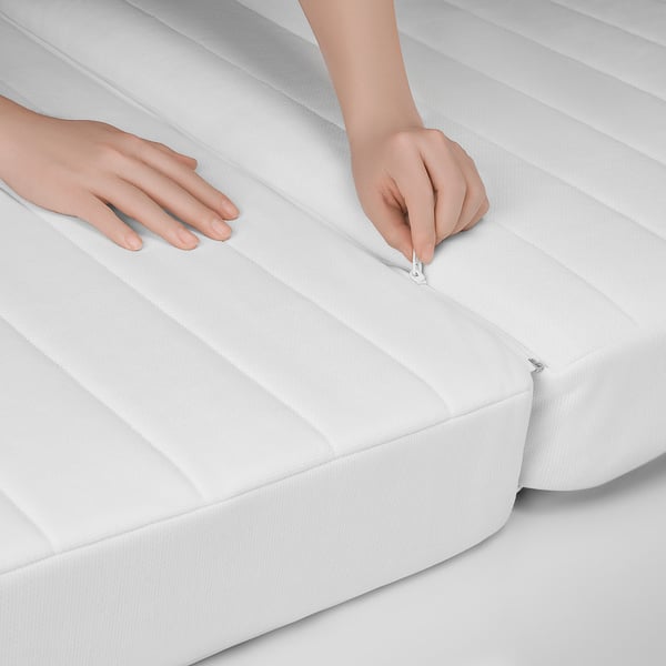 Lähikuva käsistä, jotka vetoketjuttavat puhtaan, valkoisen patjan, joka näyttää sen korkealaatuisen, sileän kankaan.