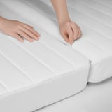 Lähikuva käsistä, jotka vetoketjuttavat puhtaan, valkoisen patjan, joka näyttää sen korkealaatuisen, sileän kankaan.