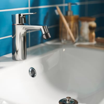 Modern badrumsblandare med elegant kromfinish på vitt handfat, mot turkosa plattor. Ergonomisk design och två inställningar för vattenläge.