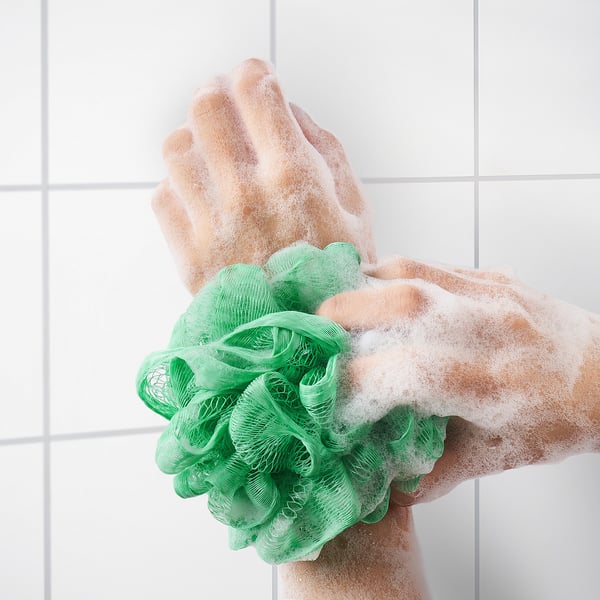 Hand med grön mesh body puff med tvål, exfolierar huden och skapar skum.