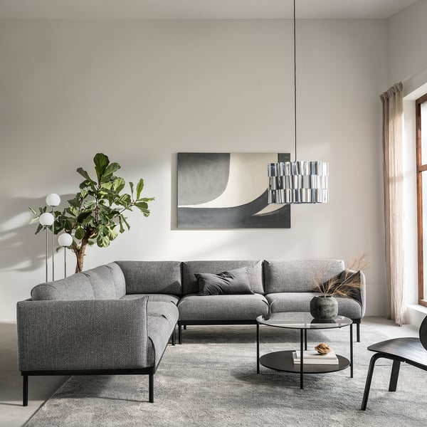 Modernt vardagsrum med grå ÄPPLARYD sektionssoffa, abstrakt konst, pendellampa, runt soffbord och stort fönster med beige gardiner.