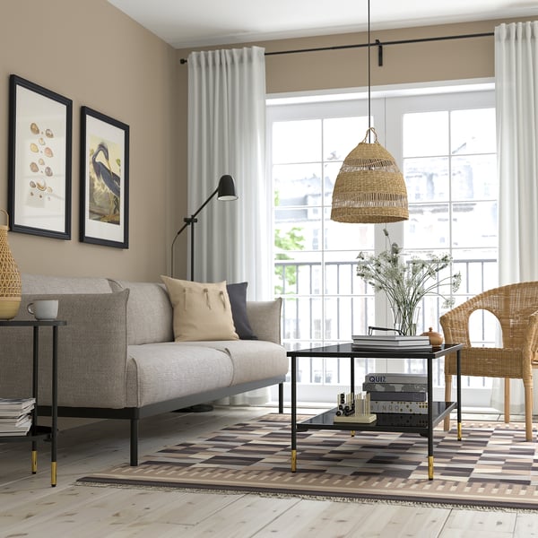 Modernt vardagsrum med grå soffa, beige matta, soffbord, konst, korgstol, stort fönster, taklampa.